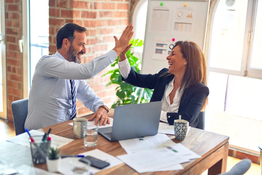 Zwei Personen in einem Büro lächeln und geben sich gegenseitig ein High-Five.